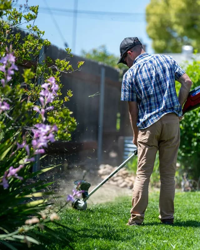 A gardener trimming a lawn edge outside a home